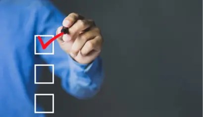 A person in a blue shirt marks a red check in a checkbox on a transparent board with a marker, symbolizing task completion or votng.